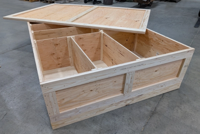 a wooden container with the lid slid off and several compartments inside sitting on a warehouse floor